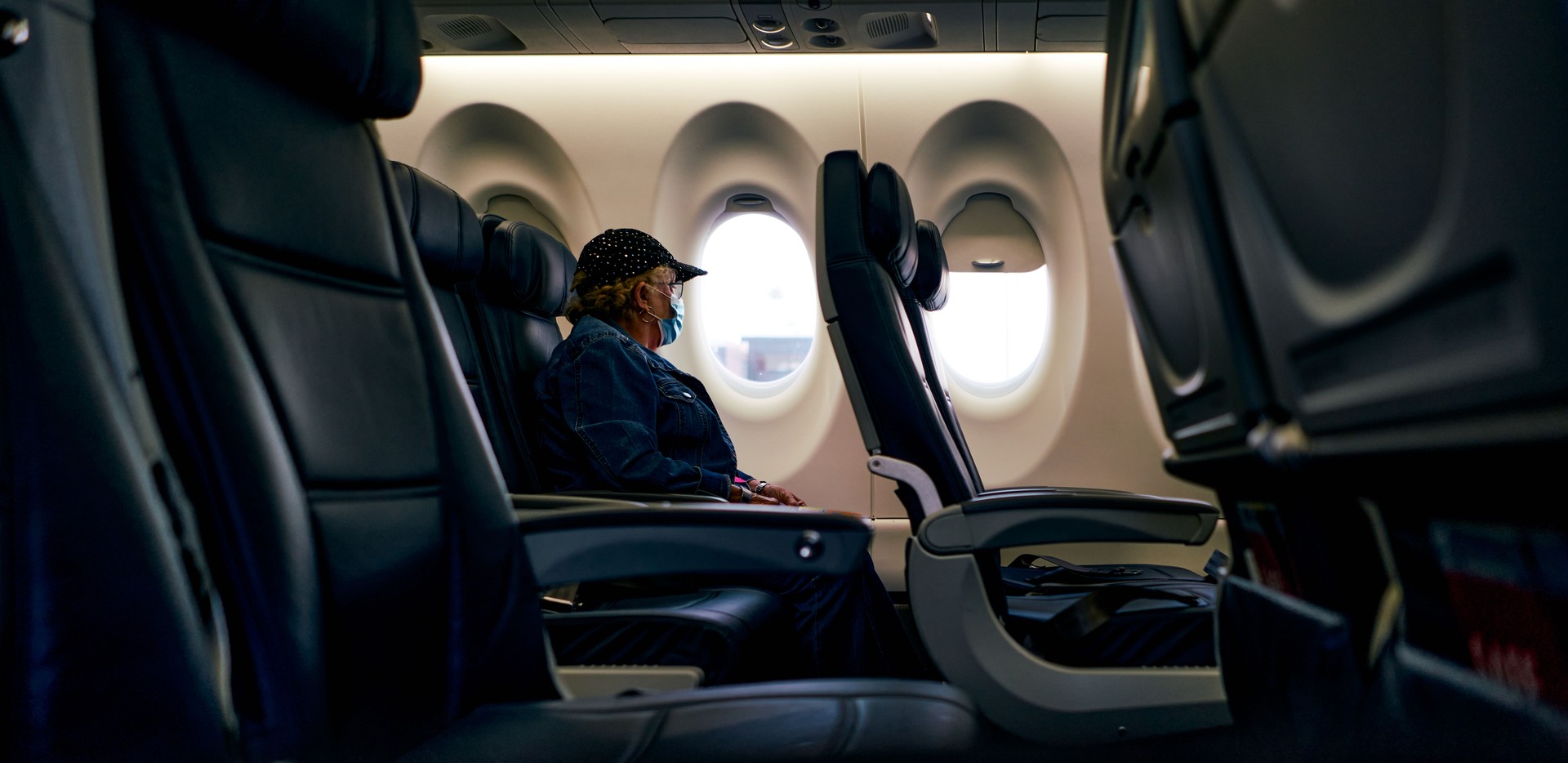 Senior woman with protective mask looking the window on a plane after coronavirus pandemic